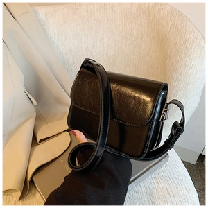Detail of black glossy patent leather crossbody bag on a textured chair with a magazine