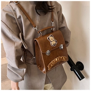 Brown vintage PU leather backpack with bear patch worn by a model on stairs