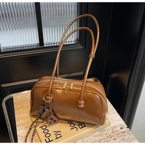 Detail of dark brown glossy leather shoulder bag with gold logo on marble surface