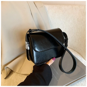 Detail view of the silver metal clasp and leather strap on a black square shoulder bag