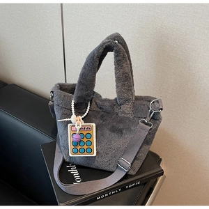 Close-up of a soft grey plush bucket bag with fuzzy handles and a cute charm
