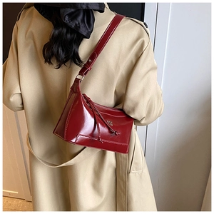 Deep burgundy leather shoulder bag detail with metal logo and fringe on a model
