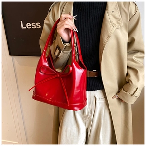 Détail d'un sac à main rouge en cuir verni avec nœud élégant et poignée arrondie chic