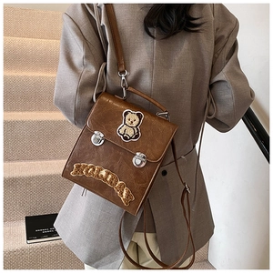 Detail of vintage brown leather backpack featuring teddy bear patch and metal buckles