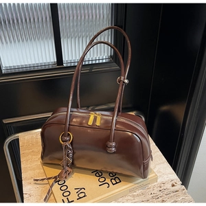 Detail of dark brown glossy leather handbag with golden zippers and braided knot charm