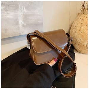 Detail of a dark brown glossy leather square crossbody bag with silver hardware on a casual setting