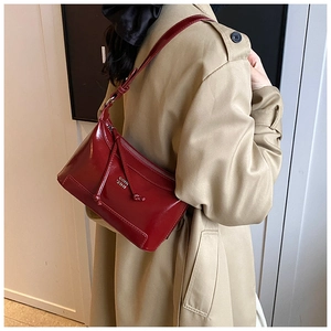 Detail of dark red patent leather shoulder bag with glossy finish and knotted strap