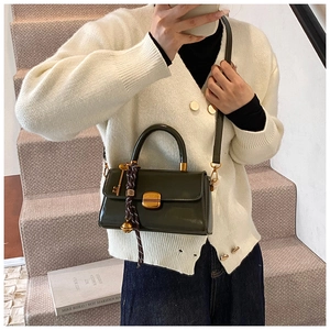 Detail of dark green patent leather handbag with gold square lock and bell pendant