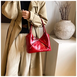 Détail d'un sac à main en cuir verni rouge vif avec un grand nœud décoratif devant