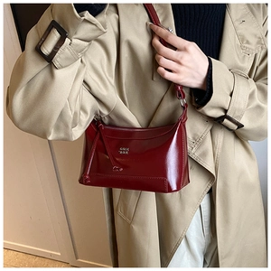 Model wearing a burgundy high-gloss shoulder bag with a sleek metal logo and retro vibe