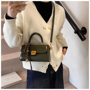Detail of dark green patent leather handbag with gold metal clasp and woven rope charm