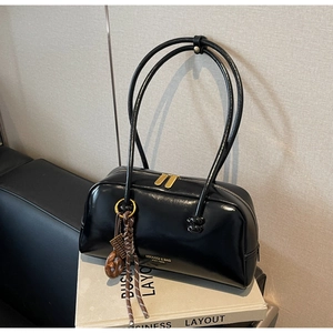 Detail of black glossy leather bowling bag with gold zipper and woven charm accessory