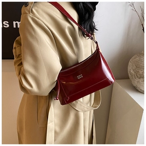 Close-up of wine red glossy patent leather shoulder bag with chic drawstring and logo details