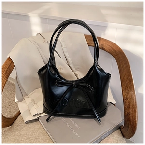 Détail d'un sac à main en cuir noir avec nœud et relief posé sur une chaise en bois