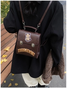 Outdoor view of a vintage brown leather backpack with teddy bear patches and metal buckles