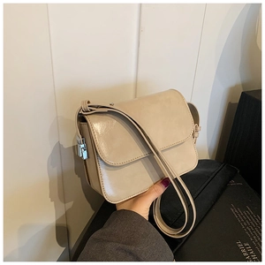 Close-up detail of beige glossy faux leather crossbody bag with silver buckle and thin strap