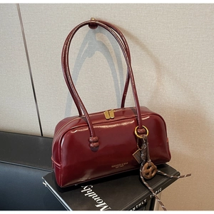 Detail of dark red patent leather shoulder bag with gold logo and vintage tassel charm