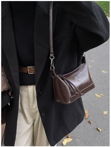 Detail of a dark brown glossy leather shoulder bag with metallic COIN logo on the side