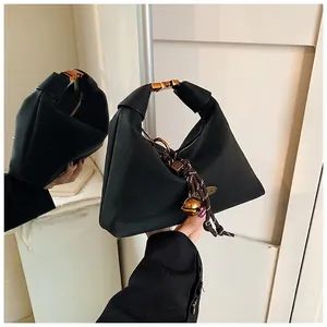 Détail du sac à main noir avec boucle dorée et pendentif clochette en corde tissée