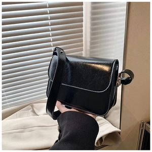 Close-up of black glossy rectangle crossbody bag featuring wide strap and sleek flap design