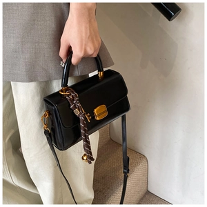 Detail der schwarzen glänzenden Handtasche mit goldenem Schloss und Glockenanhänger