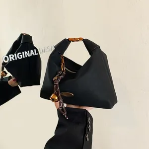 Détail du sac fourre-tout triangulaire noir avec boucle dorée et breloque en cordelette
