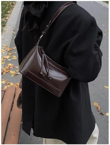 Detail of a dark brown glossy pillow shoulder bag featuring metallic logo and street style look