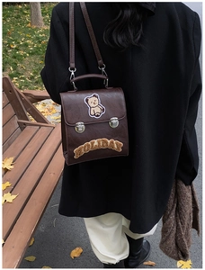 Detail of a dark brown faux leather bag with a plush bear patch and holiday embroidery