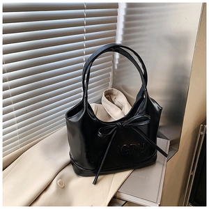 Détail d'un sac cabas en cuir brillant noir avec nœud et lettres embossées