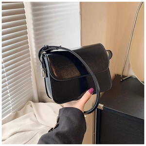 Detail of a black glossy leather square crossbody bag with a flap closure and strap