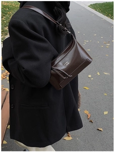 Dark brown faux leather pillow bag with silver logo worn with a black winter coat