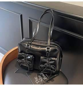Detailed view of black glossy tote bag featuring decorative bows and twin front pockets