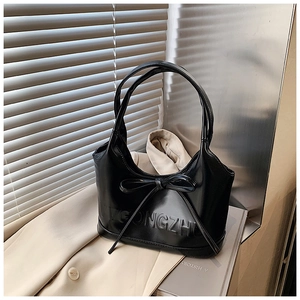 Détail d'un sac à main en cuir noir brillant avec un nœud et un lettrage en relief