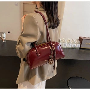 Detail view of burgundy shiny leather boston bag with gold zipper and stylish tassel