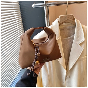 Détail du sac en cuir marron avec poignée nouée et plaque métallique de fabrication artisanale