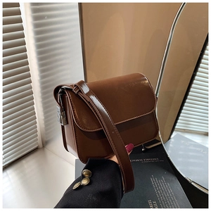 Detail of a deep brown glossy leather crossbody bag with a metallic closure and strap