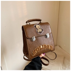 Detail of vintage brown leather backpack featuring a plush bear patch and holiday embroidery