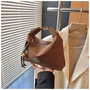 Détail d'un sac à main marron avec plaque métallique handmade et pendentif clochette