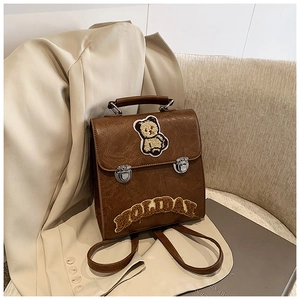 Detail of vintage brown backpack featuring cartoon bear embroidery and plush HOLIDAY lettering