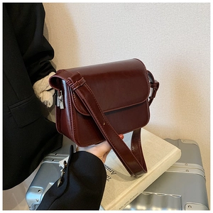 Close-up of a burgundy glossy square crossbody bag with silver hardware and shoulder strap