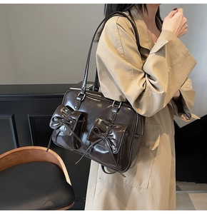 Detail of dark brown patent leather tote with two bow-adorned front flap pockets