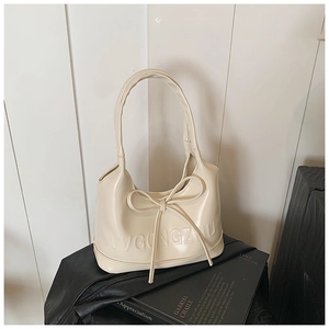 Détail d'un sac à main beige brillant avec nœud 3D et logo embossé sur le cuir PU