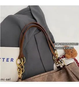 Detail of brown canvas tote bag with leather strap, gold chain links, and plush bear charm