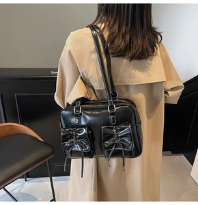 Detail of black tote bag with white stitching and bow-tie pockets on soft beige trench coat