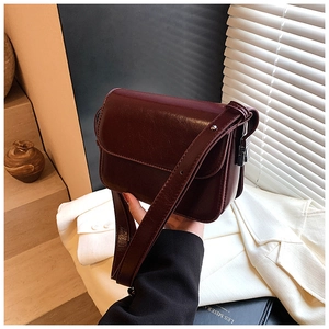 Detail of wine red glossy leather crossbody bag showing side buckles and strap