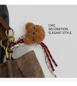 Detailed view of a plush bear bag charm with woven tassels on a canvas shoulder strap