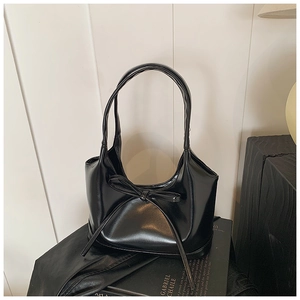 Détail d'un sac sous le bras noir brillant avec nœud décoratif sur un support de livre