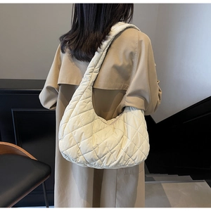 Detailed view of cream quilted hobo bag styled with a trench coat on a model's shoulder