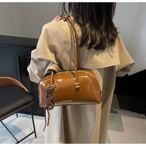 Detailed close-up of glossy brown faux leather shoulder bag with decorative woven rope charm