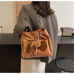 Detail of a brown suede tote bag featuring a gold chain strap and a plush bear charm